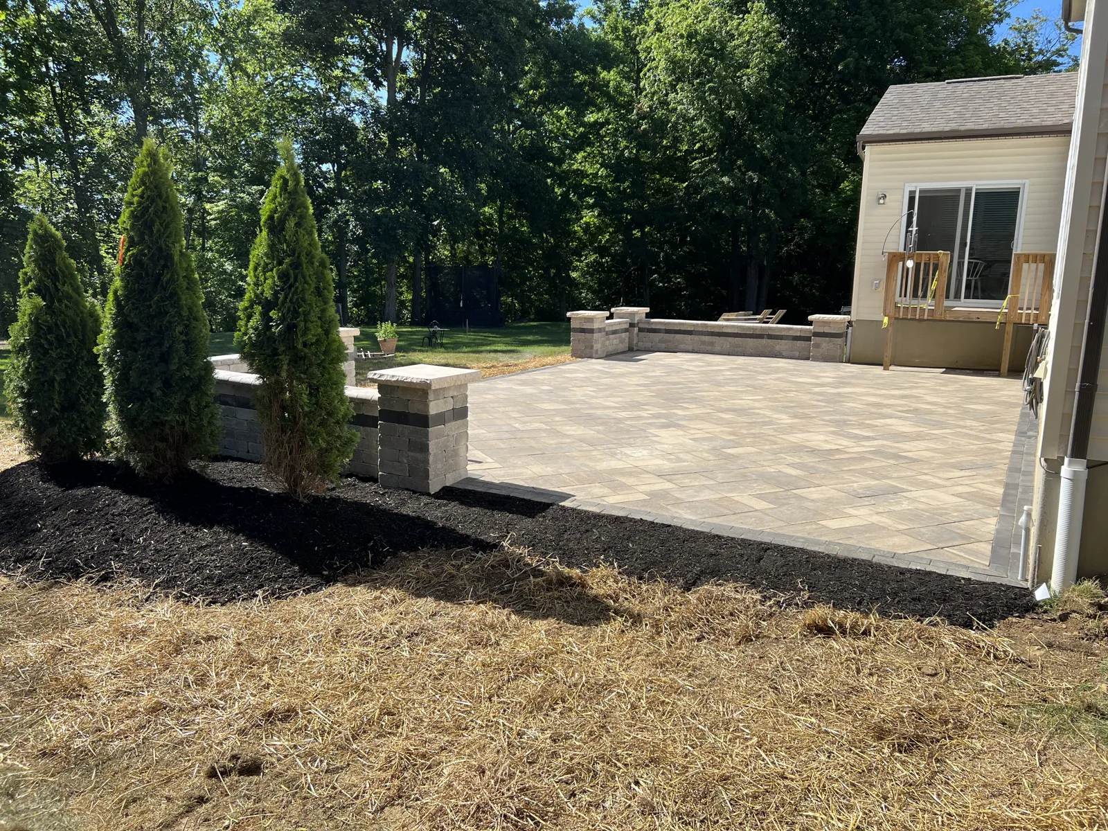 Paver patio framed by stone pillars and evergreens