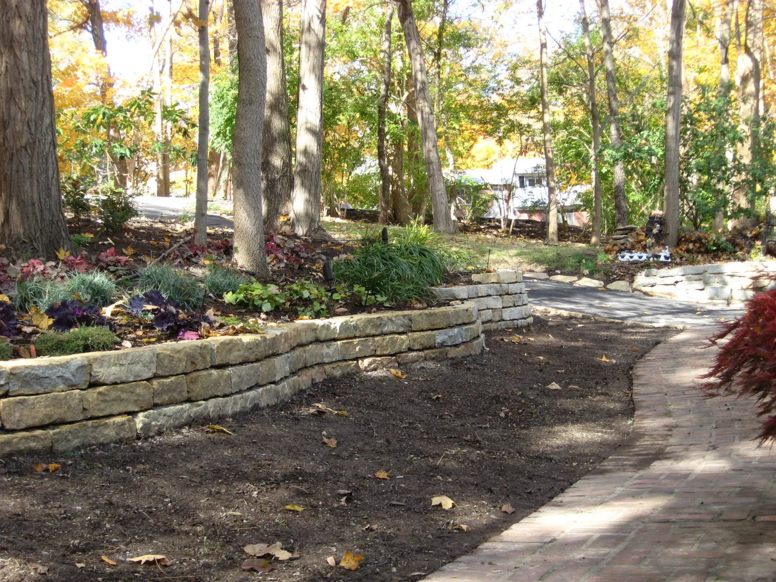 Low limestone wall following a curved paver walk through the trees