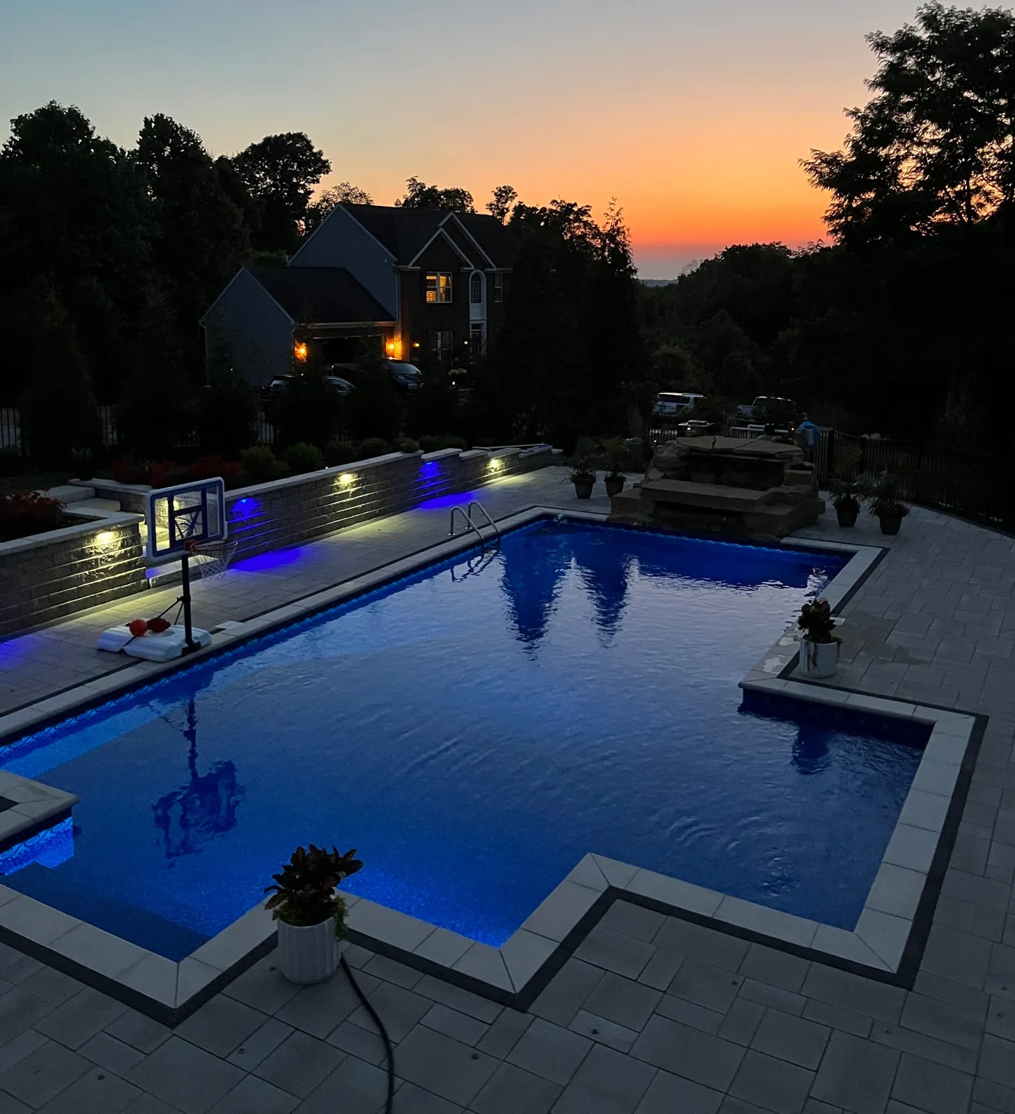 Pool glowing at dusk with illuminated stone retaining walls, built by TJs Landscaping in Milford, Ohio