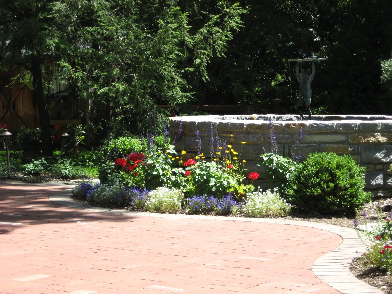 Brick patio edged by perennial flowers and a stone fountain wall