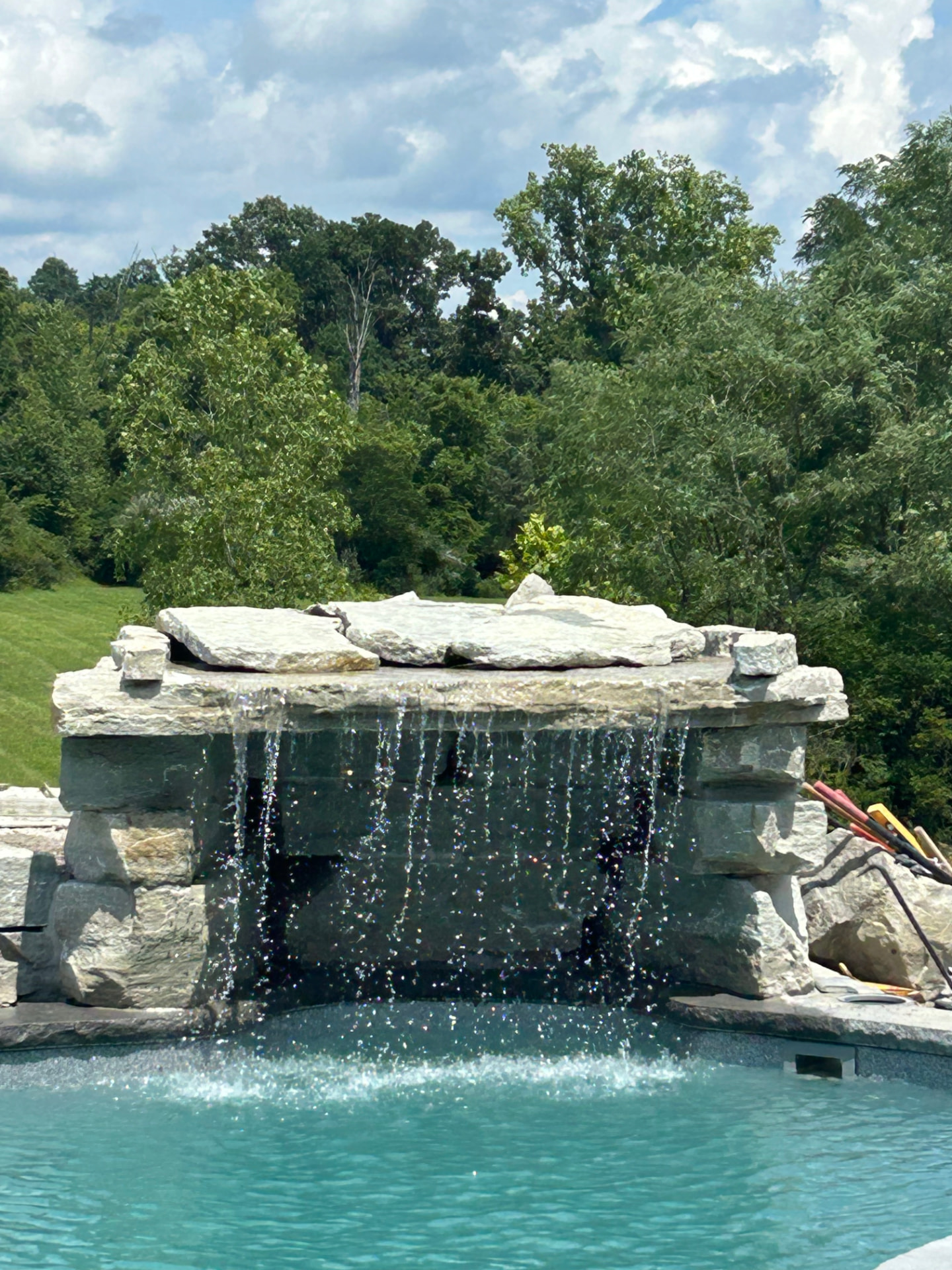 Stacked natural stone waterfall spilling into a blue pool