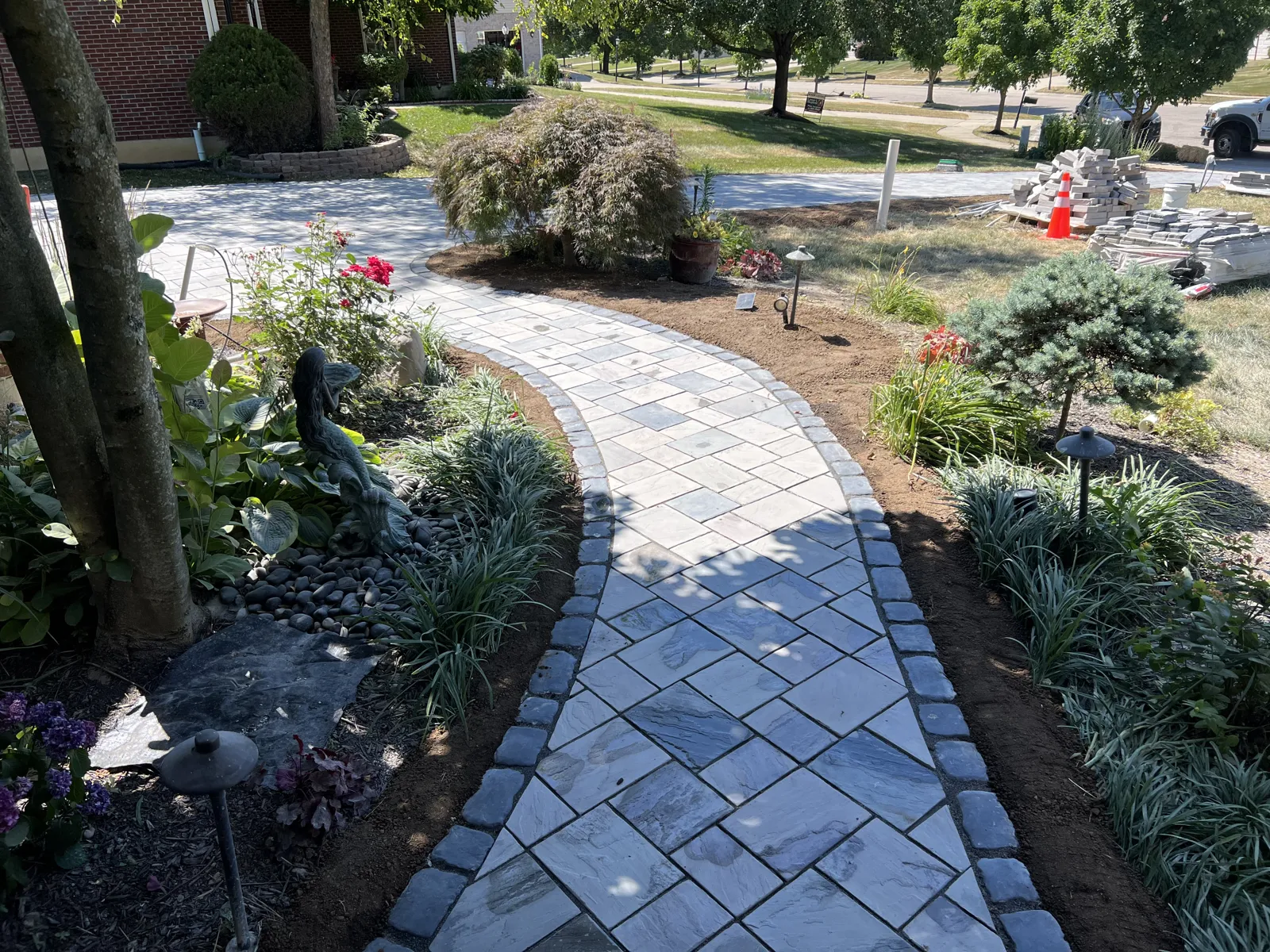 Curving paver walkway with charcoal border through lit perennial gardens