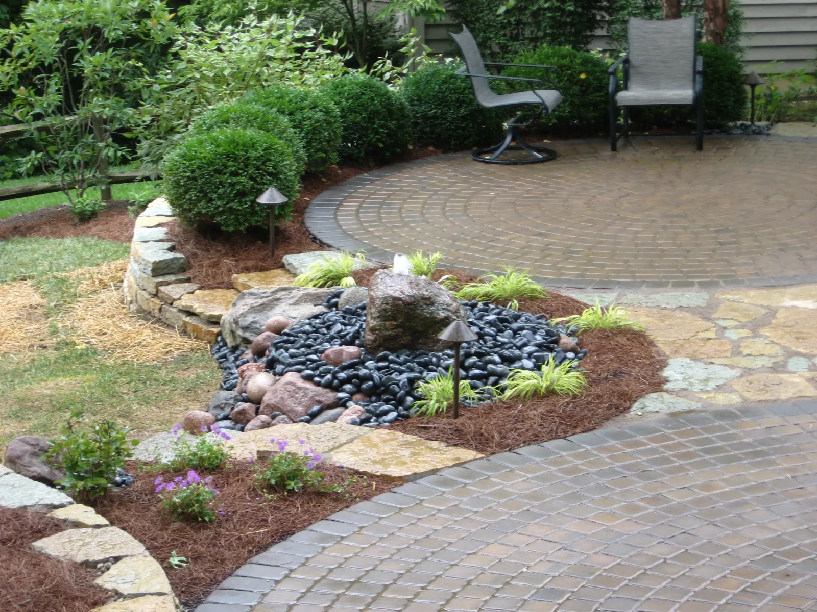 Paver patio seating area beside a boulder and river rock fountain