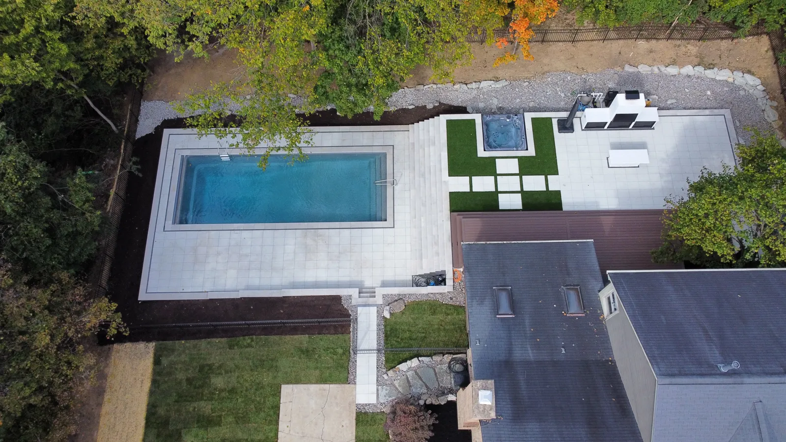 Drone view of a large paver pool deck, sunken hot tub with turf inlays and grill terrace