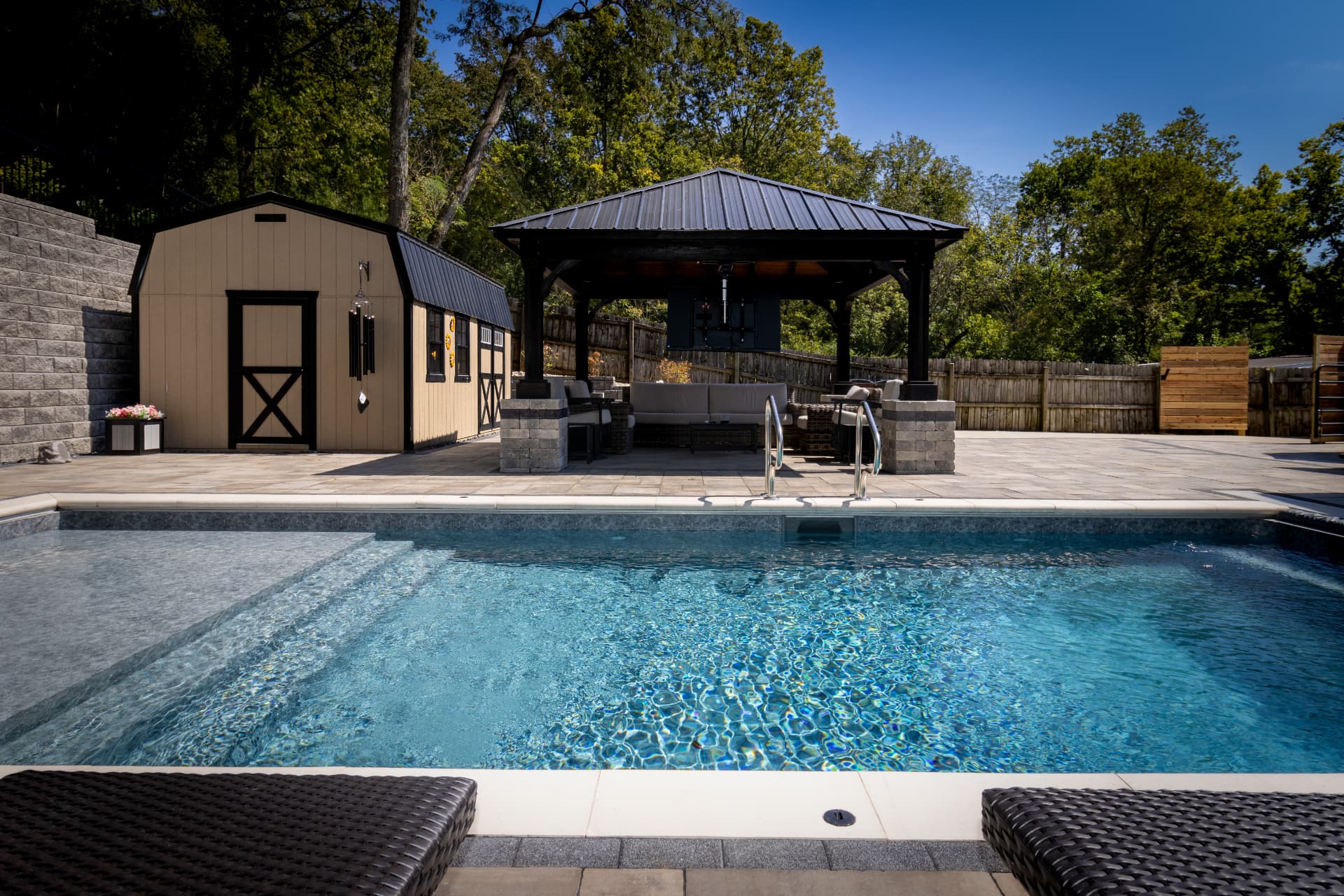Rectangular pool with tanning ledge, paver deck and black metal roof pavilion