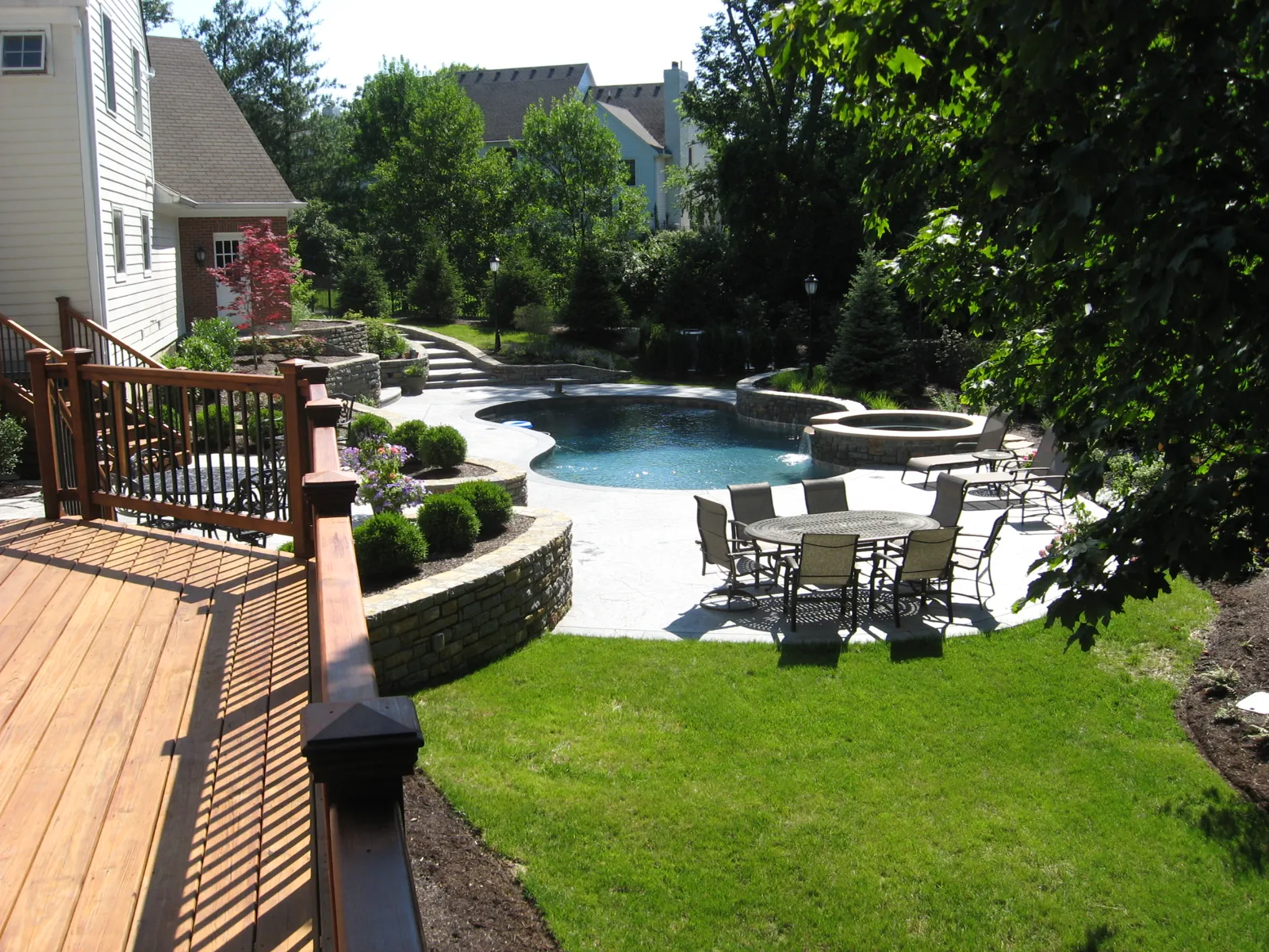 Overview of deck, pool, stone walls, patio dining and lawn
