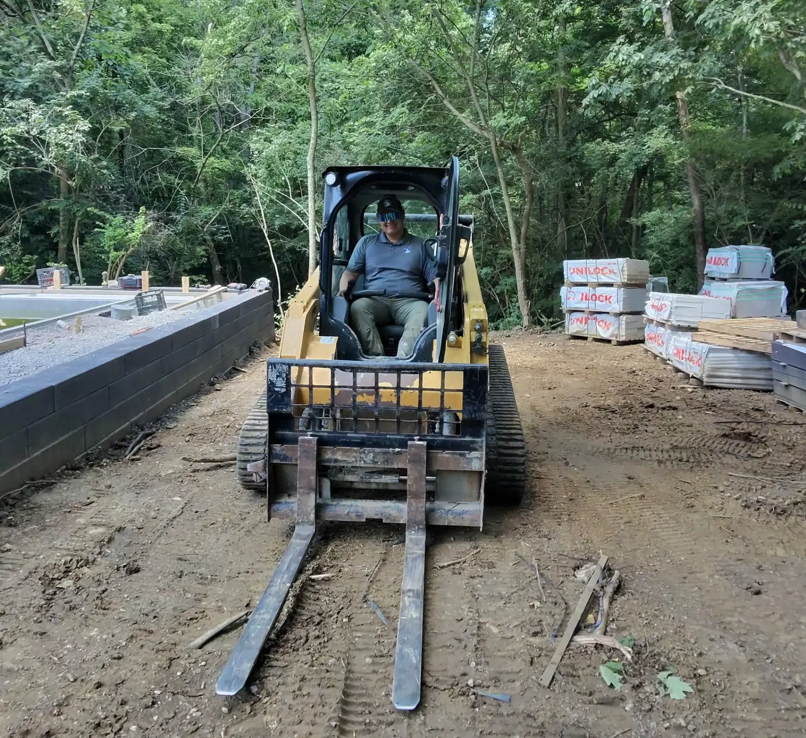 Design-Build Project Manager Alex operating a tracked loader beside Unilock materials